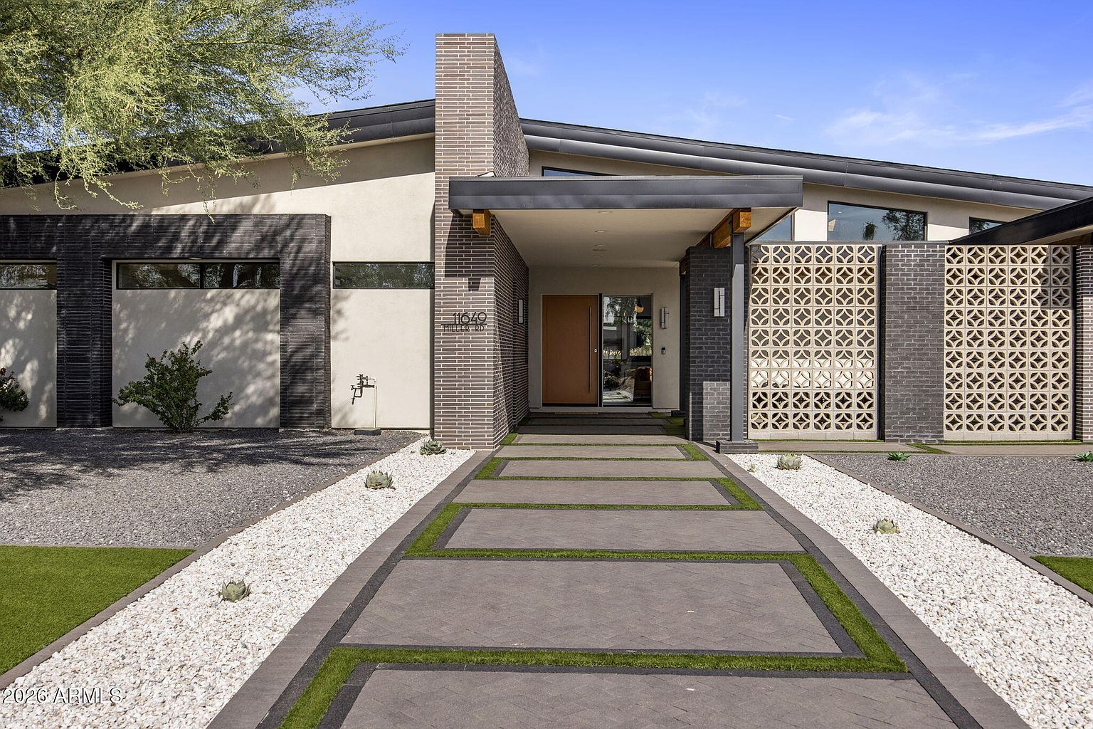 Entry walkway by daylight: paver stones, breeze-block screen on the right, mid-century-modern brick chimney and steel beam roofline framing the front door.
