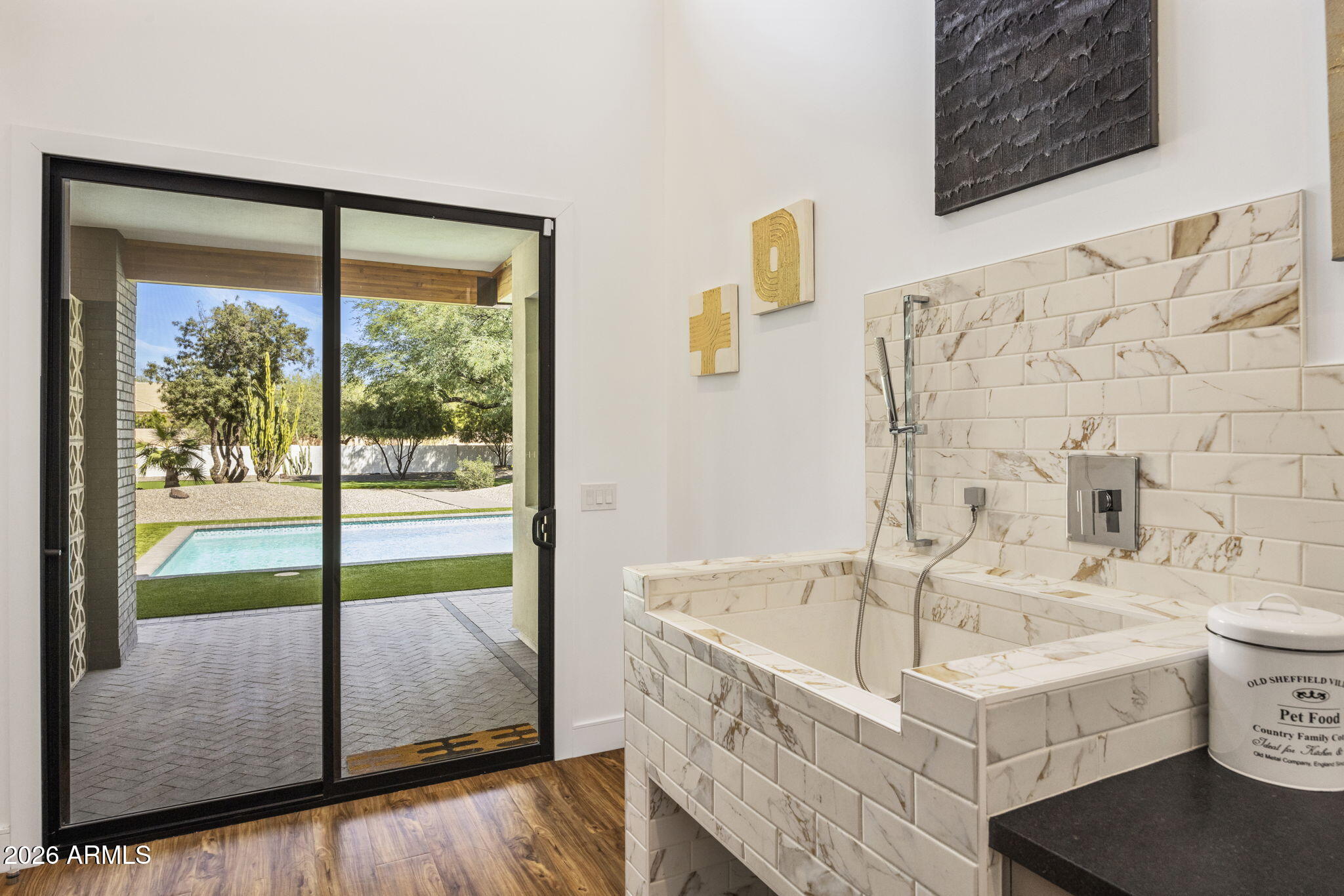 A primary bath in Calacatta marble: an oversized soaking tub, a wall-mounted spa shower, and a sliding glass door opening directly onto the pool deck.