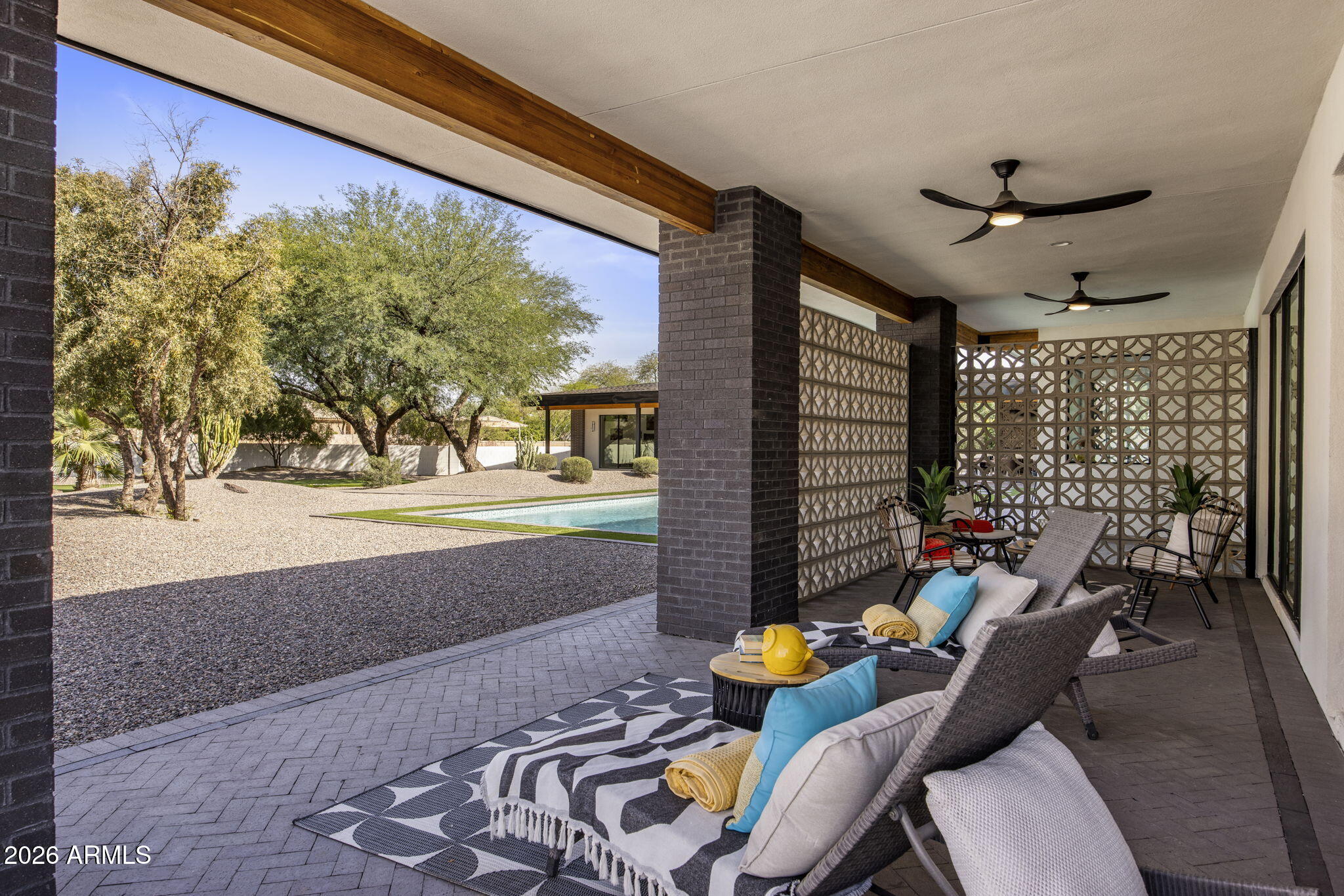The covered patio off the great room: brick columns, breeze-block privacy screen, an overhead fan, lounge chairs facing the pool, and the desert garden beyond.