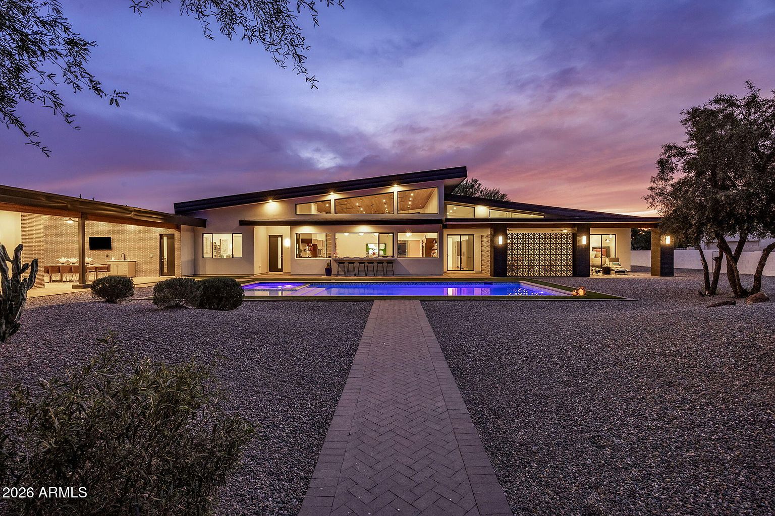 Twilight view of the resort-style backyard at 11649 N Miller Road, Scottsdale: heated pool, mid-century-modern facade lit from within, dramatic Sonoran sky.